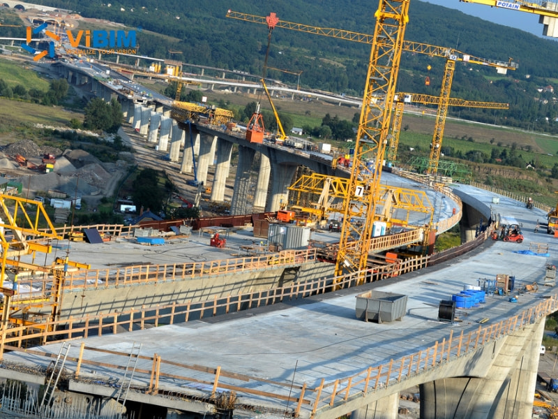 Highway bridge construction site with yellow cranes and concrete foundations