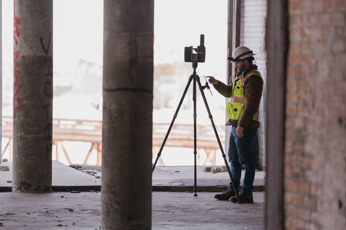 Surveyor operating a laser scanner on a tripod inside an unfinished building to capture a point cloud